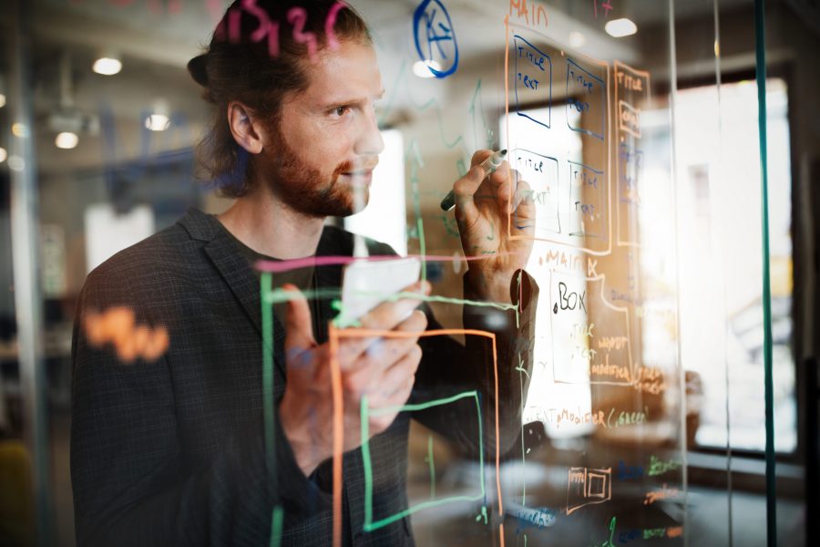 Handsome,Man,Working,And,Writing,On,Glass,Board,In,Office.